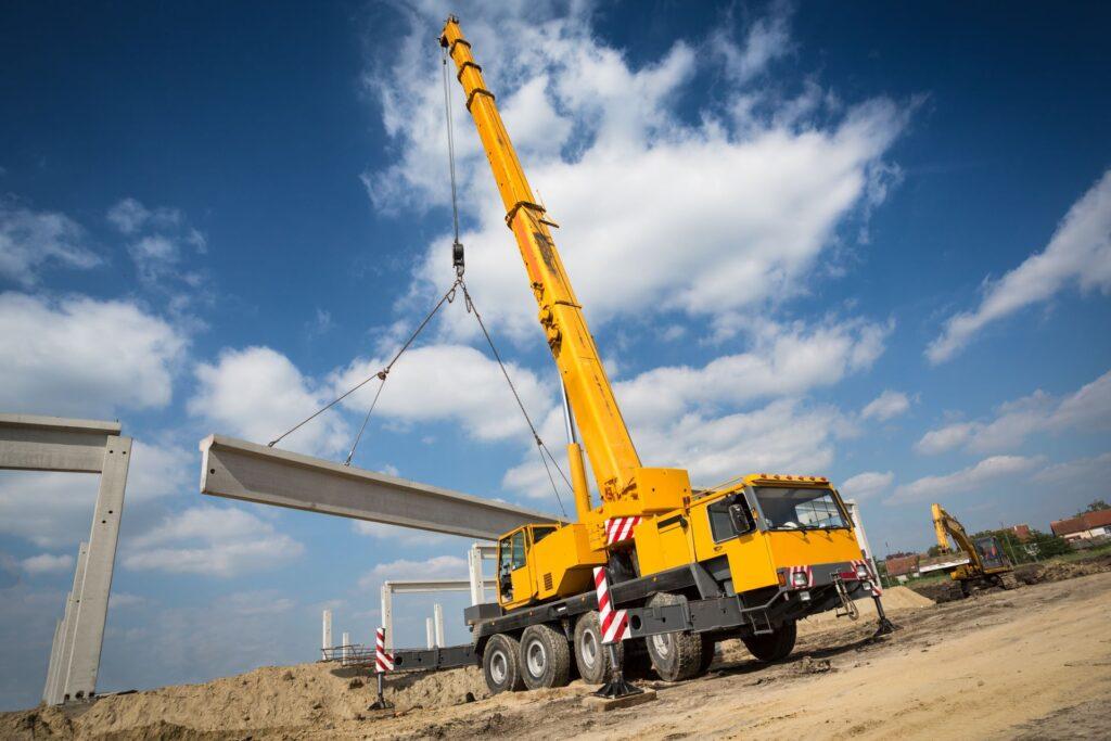 Gelber Kran hebt Betonträger auf Baustelle